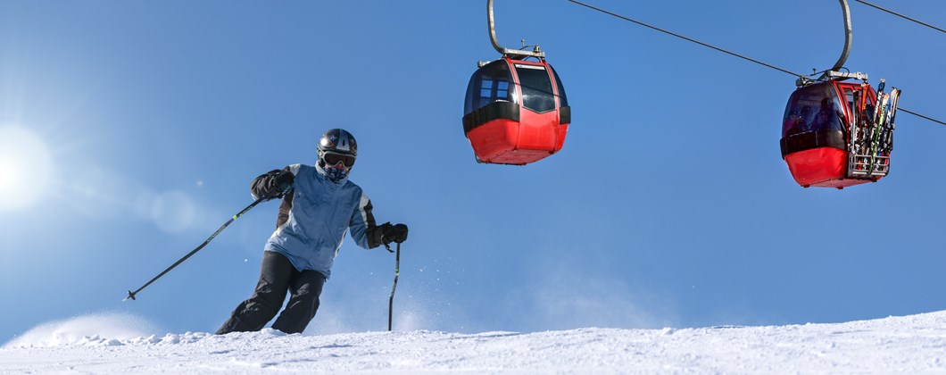 Man skiing down a snow slope with ski-lift carriages in the background.