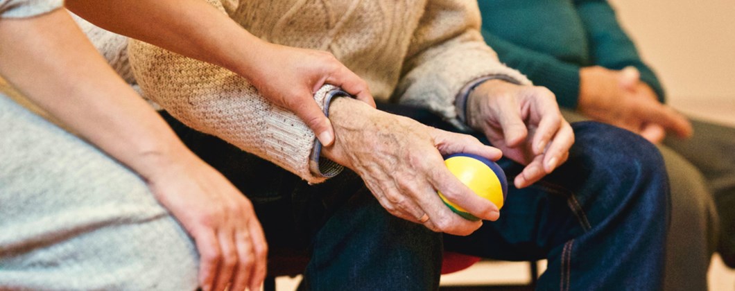Elderly person holding a ball in a care home.